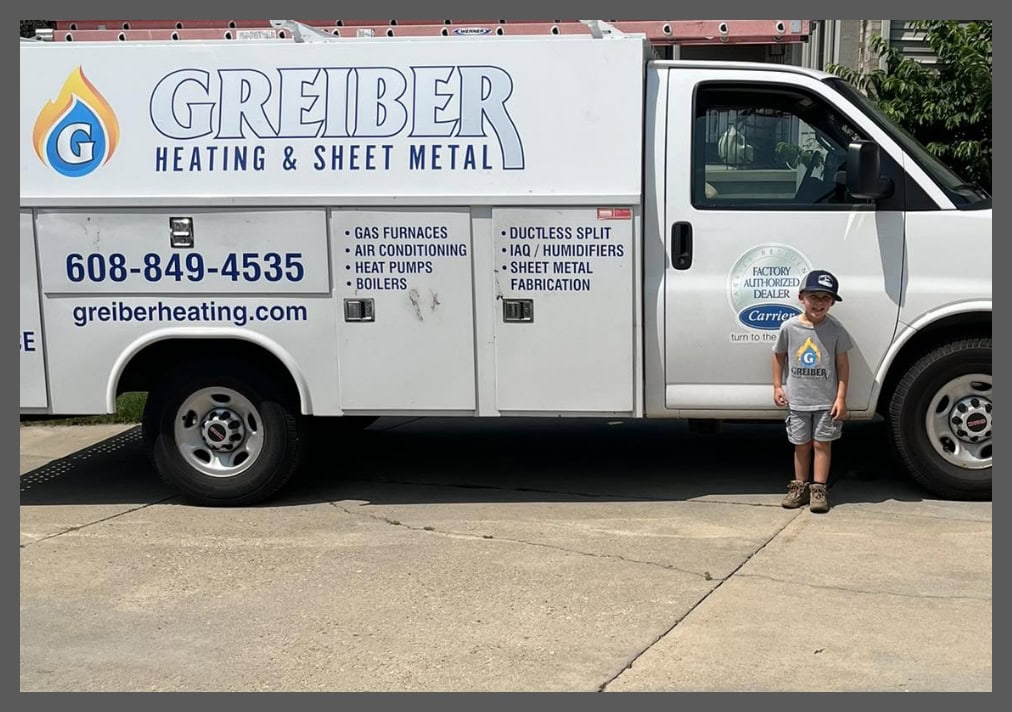 Young boy standing in front of Greiber Heating & Sheet Metal service vehicle, outside Waunakee, WI, office.