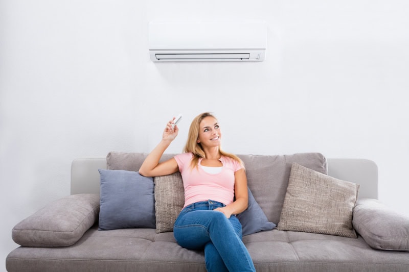 Female homeowner sitting on her couch in Waunakee, Wisconsin, adjusting the ductless mini split mounted to wall.